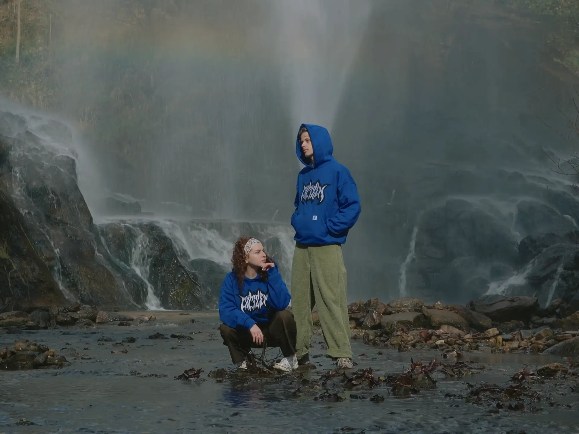 jeune couple au milieu d'un ruisseau posent avec deux pulls bleus ça fait penser à une publicité de vêtements