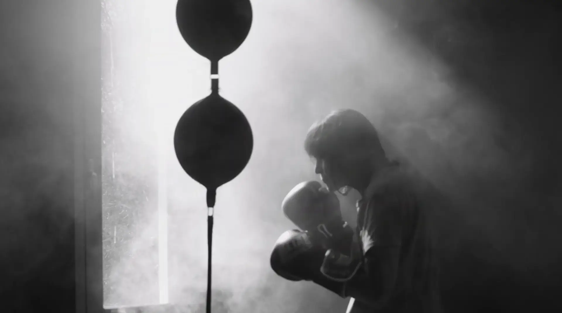 vielle dame entrain de taper dans un punching ball, elle est de profil, l'image est en noir et blanc ce qui donne une ambiance très cinématique