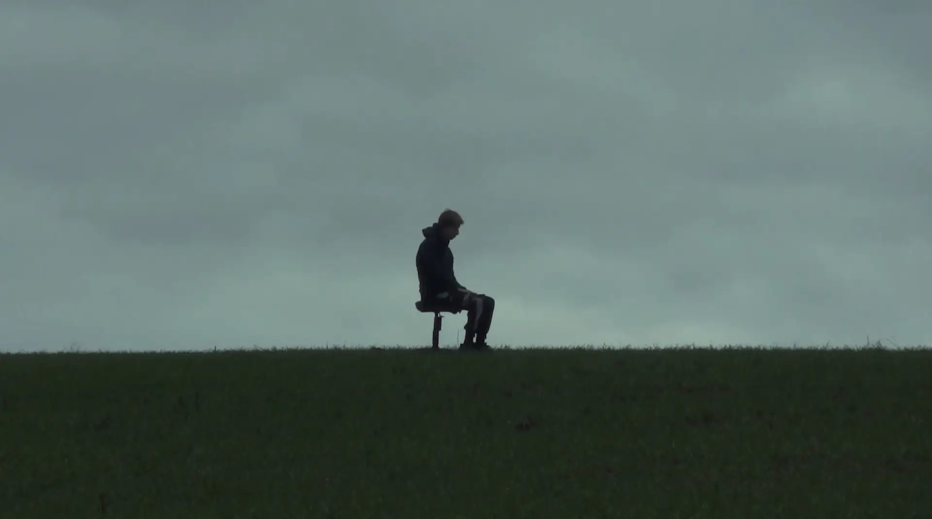 jeune homme en haut d'une colline de profil, ciel gris et ambiance assez triste