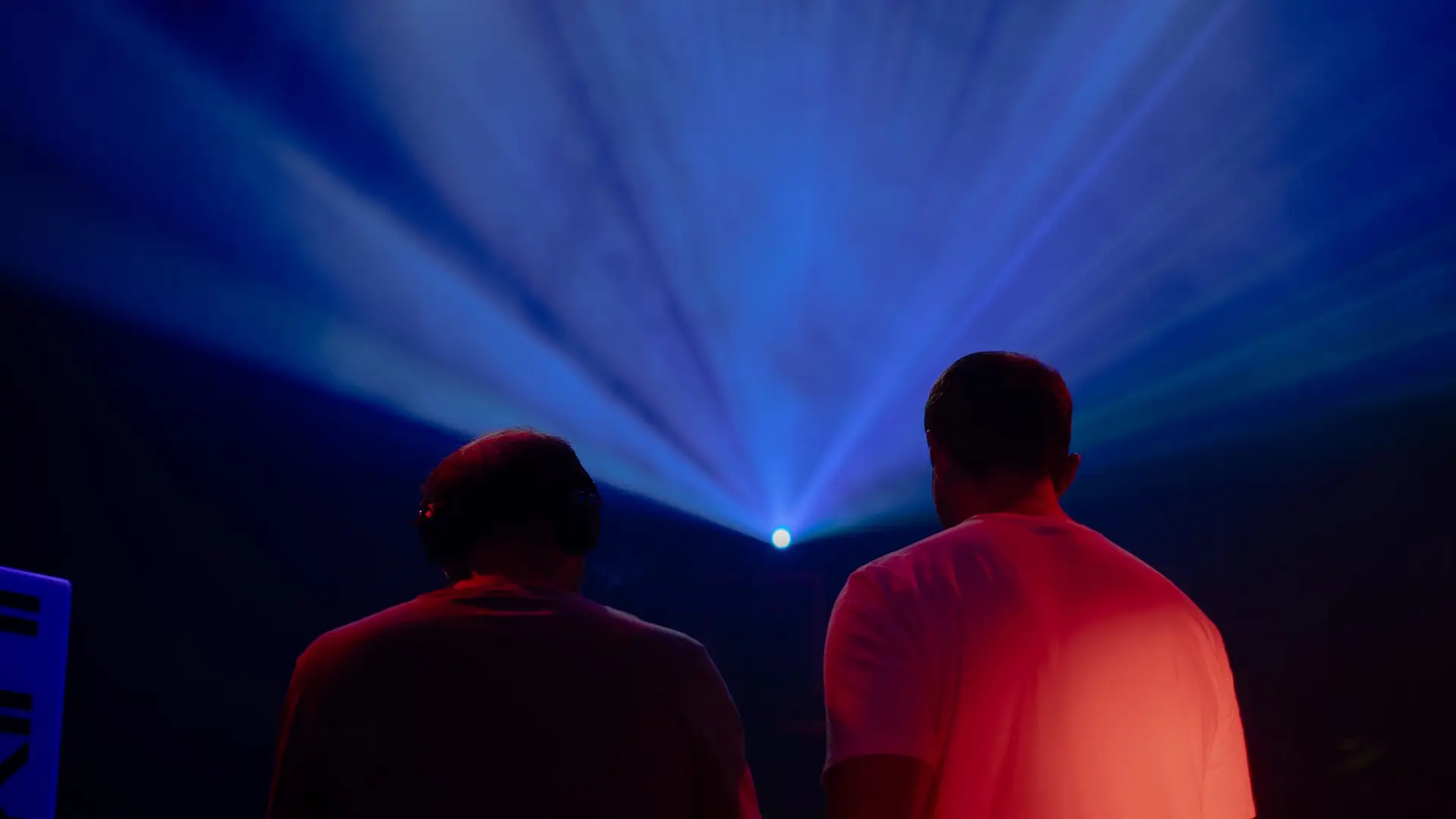deux hommes de dos ambiance de soirée en club, on comprend que ce sont des dj la composition de l'image est très équilibrée