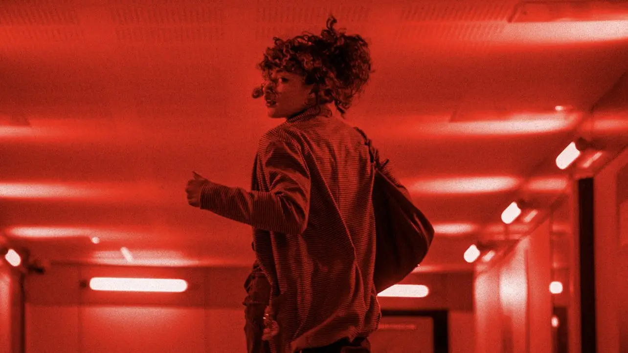 jeune femme entrain de courir dans un couloir rouge on ressent la pression et le danger dans sont attitude