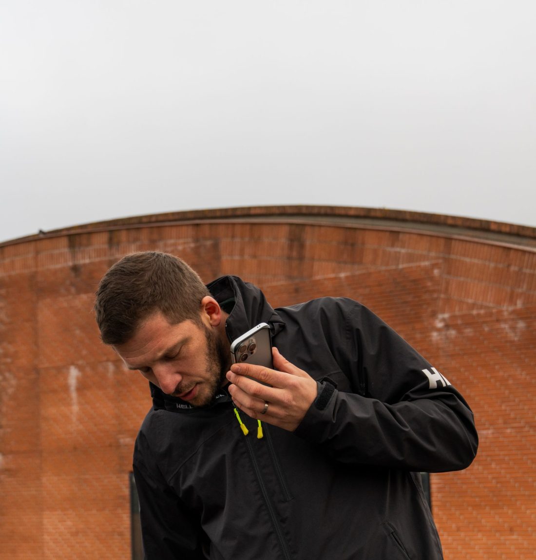 Ludovic de LP-Ventil est au téléphone avec un client. Il est dehors un mur de brique rouge est présent derrière lui.