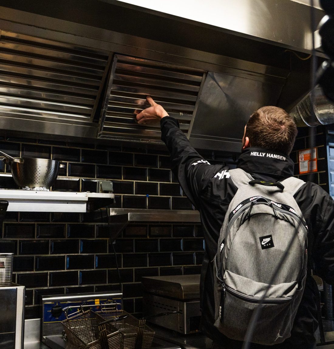 Ludovic de LP-Ventil est entrain d'inspecter une ventilation déjà existant qu'il devise pour la remplacer car elle est défectueuse. Nous sommes dans une cuisine de restaurant avec les friteuses et ustensile de cuisine.