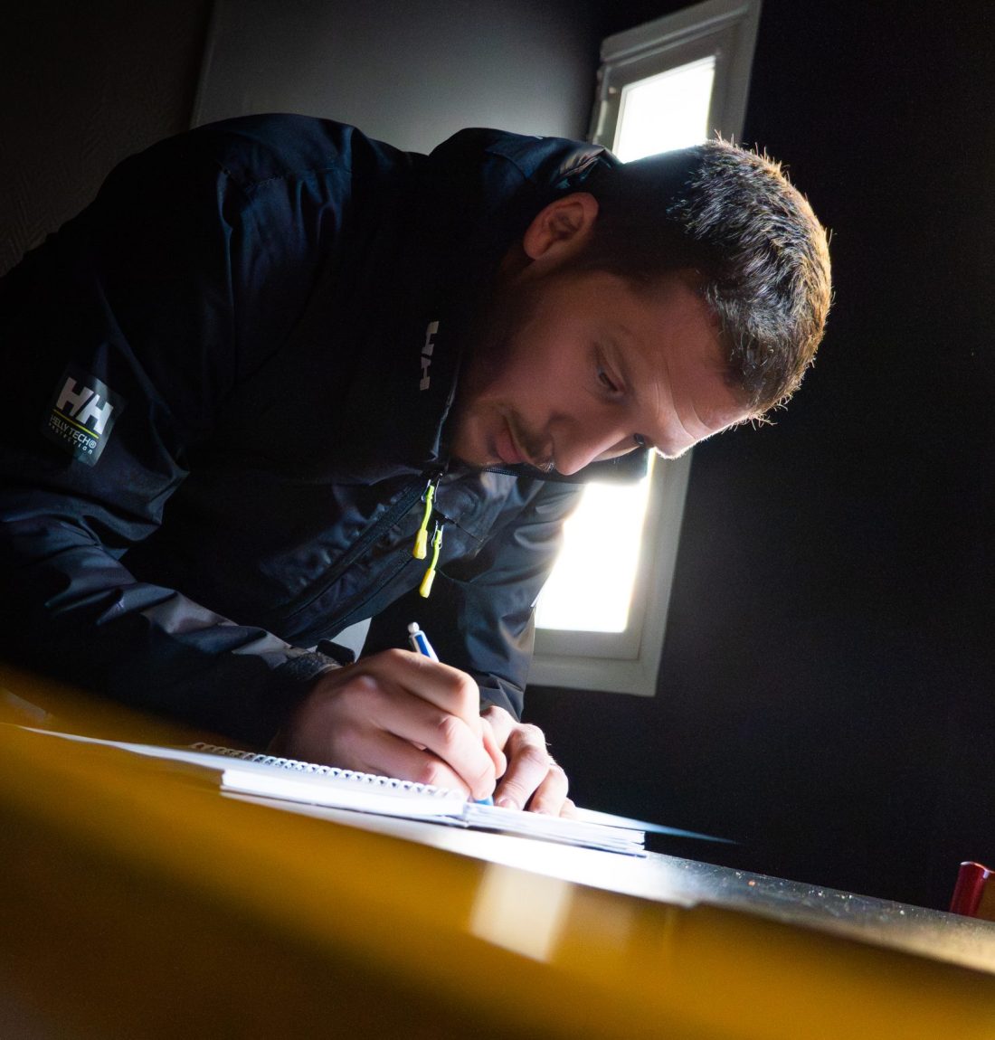 Ludovic de Lp-ventil après un rendez-vous dans un restaurant pour le remplacement d'une ventilation, il prend des notes sur son carnet afin de pouvoir faire un devis au client. Il le fait sur une table du restaurant, avec la lumière qui sort d'une fenêtre en arrière plan qui le fait ressortir.