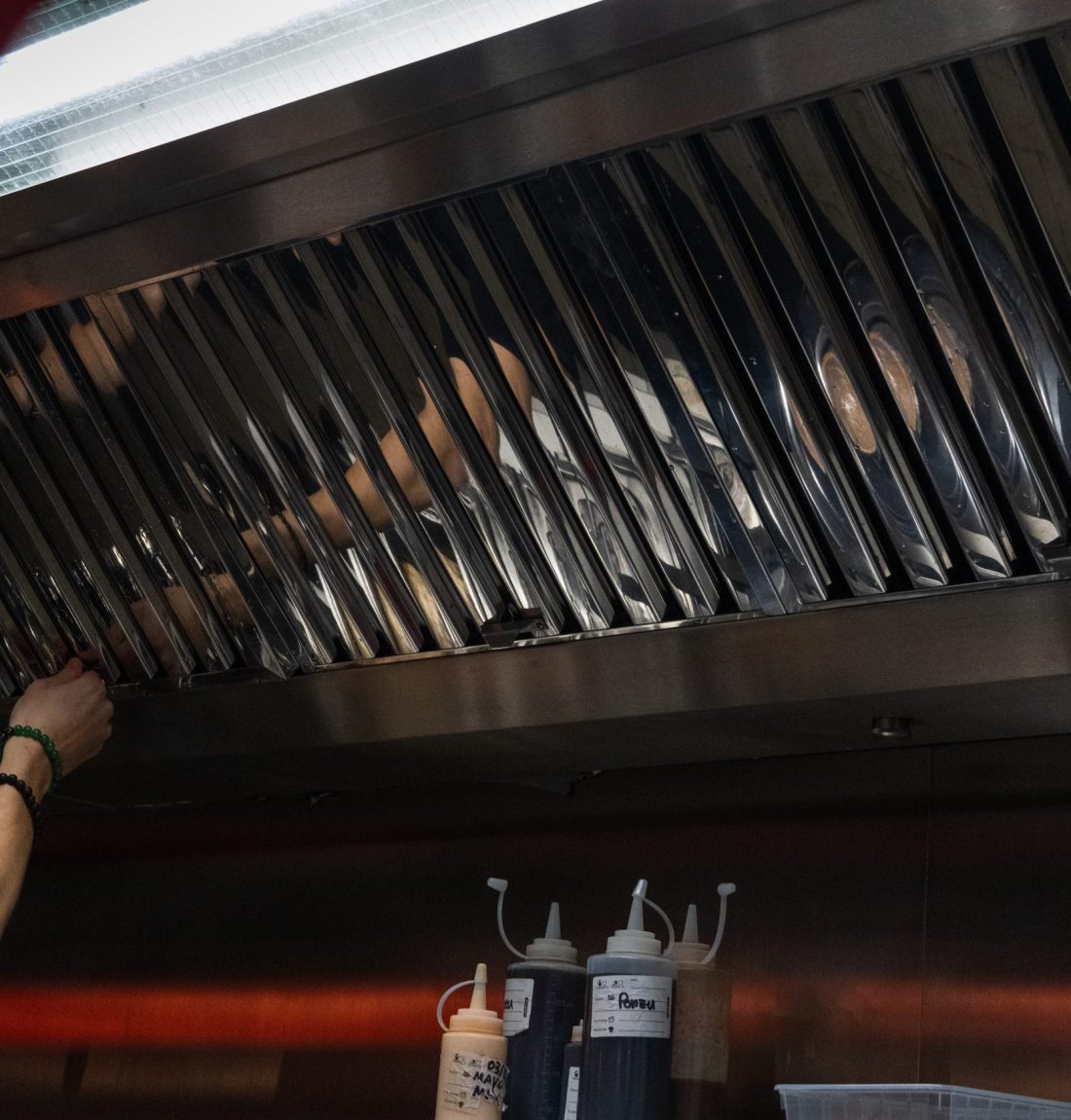Nous sommes dans un restaurant où la ventilation des cuisines est faites par LP-Ventil. Les tons rouges ressortent de l'image. Il y a une personne qui remets une des grilles de la ventilation après l'avoir nettoyé.