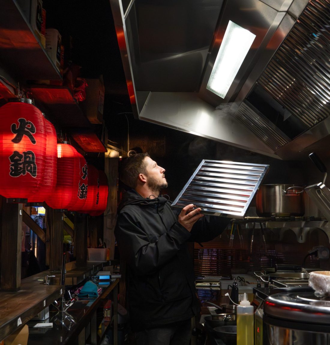 Ludovic de Lp-Ventil est entrain de regarder une ventilation qui l'a déjà installé dans une cuisine d'un restaurant japonais à Toulouse. On reconnait sur la gauche la décoration de rue japonaise du restaurant toulousain Yujo Ramen. Ludovic est dans la cuisine en regardant la ventilation sur la droite de l'image.