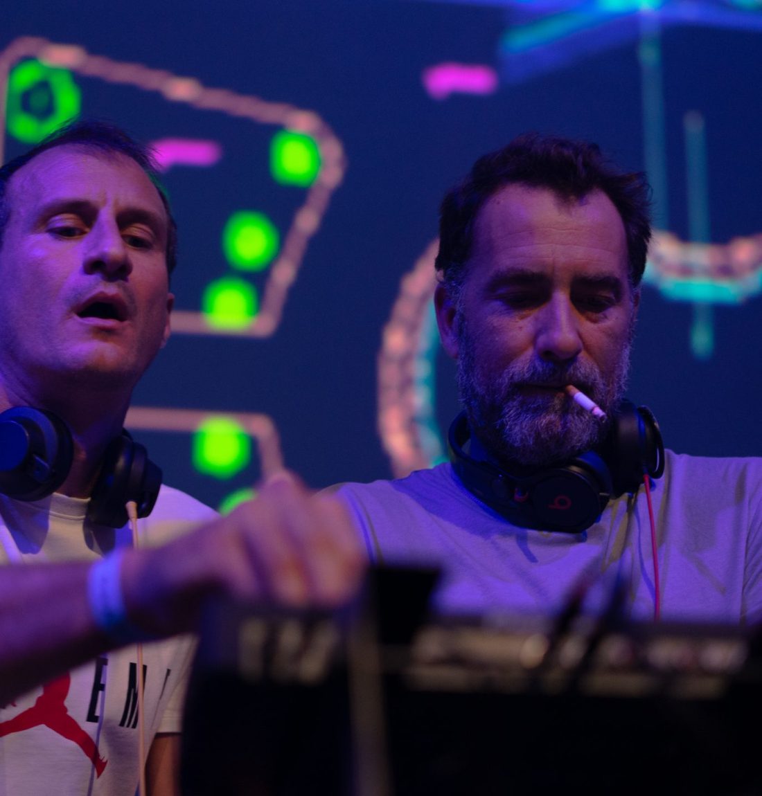 Les deux dj du groupe The Deep Brothers sont entrain de mixer devant un écran led en concert les deux mixent ensemble l'un à une cigarette à la bouche.