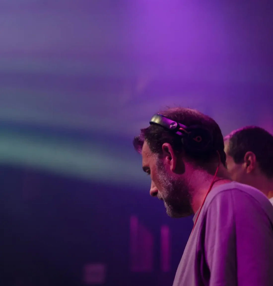 Un des deux membres du groupe The Deep Brothers est entrain de mixer il a un casque beats sur la tête et touche avec ses mains la table de mixage. Les couleurs des lum!ères ont des tons violets.