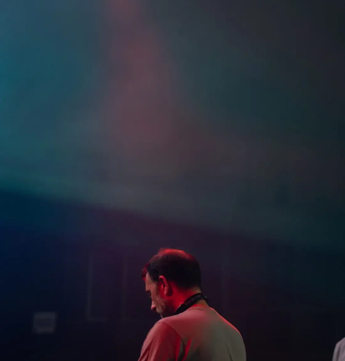 Un des deux membres du groupe The Deep Brothers est au platine de 3/4 dos les lumières sur lui sont rouge et verte.
