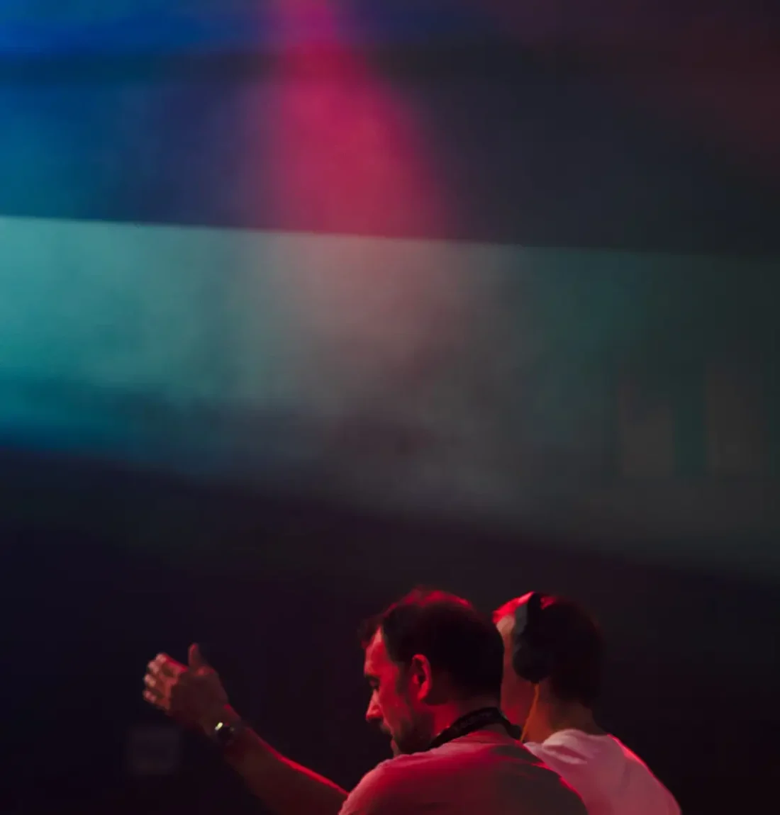 Le groupe The Deep Brothers est entrain de mixer celui derrière danse et l'autre à les mains au platines. Les lumières sont très colorés, du rouge du vert et du bleu domine.