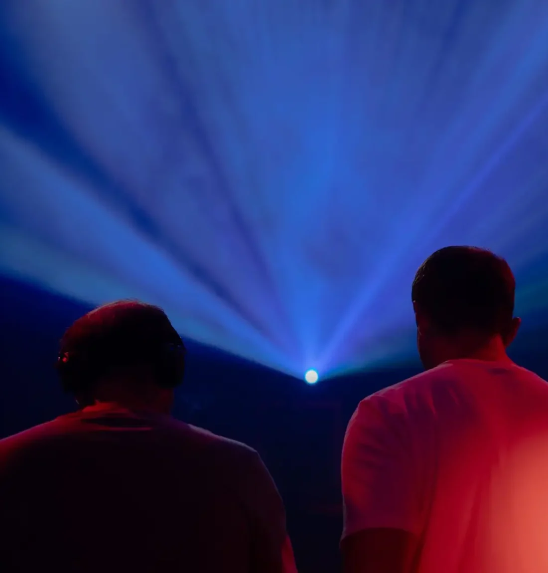 deux hommes de dos ambiance de soirée en club, on comprend que ce sont des dj la composition de l'image est très équilibrée