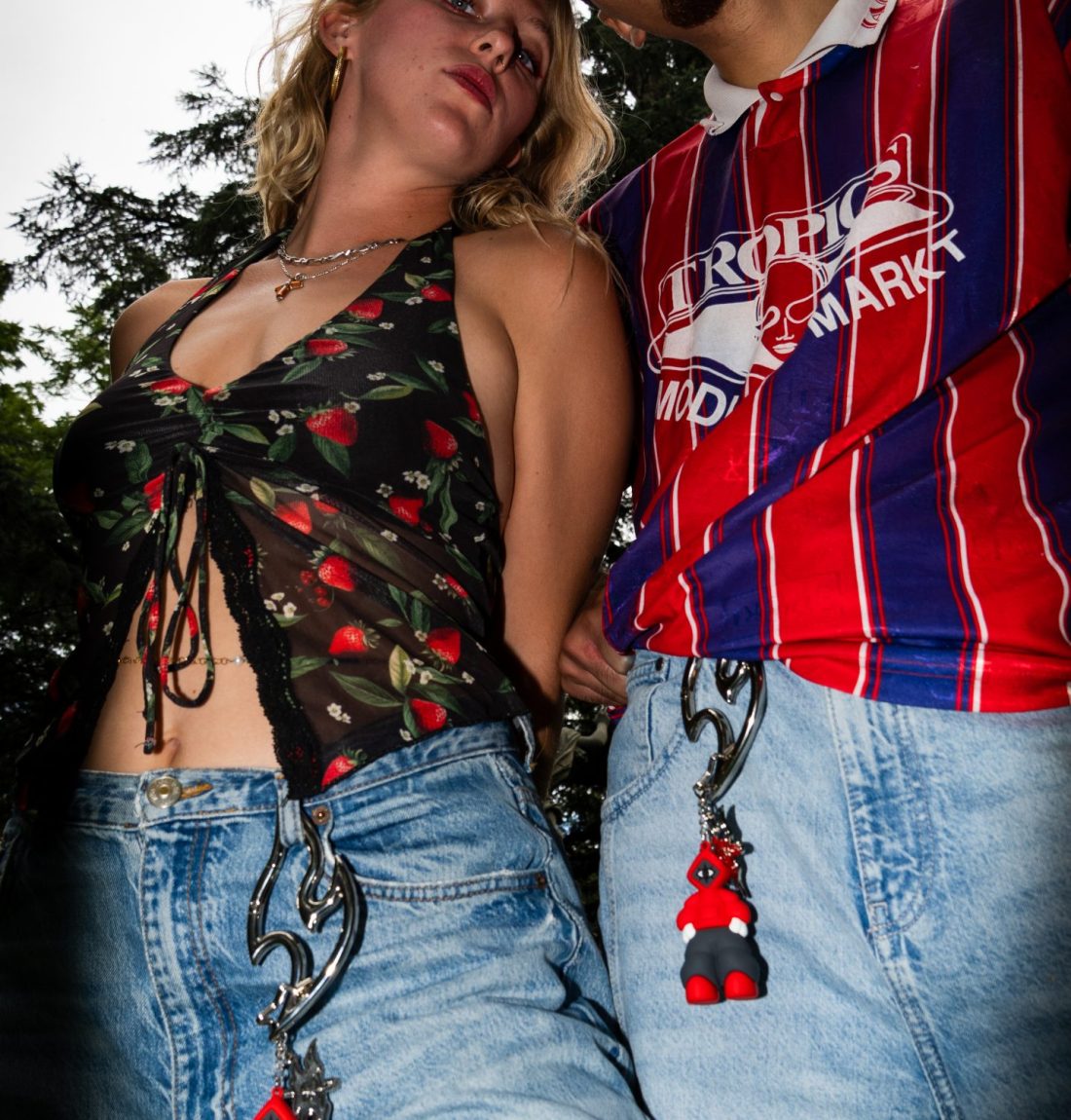 Un couple regarde la caméra et porte eux deux à leurs jean un mousqueton avec une forme peu commune avec accroché deux portes-clefs de la marque citizen représentant le logo et la mascotte de la marque.
