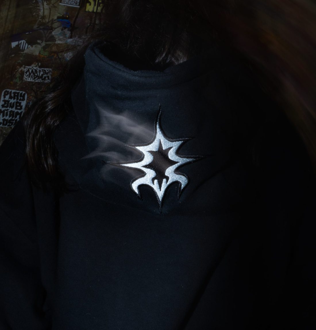 Une photo avec un flou artistique, avec un cadrage serré sur le détail de broderie du sweat noir de la marque citizen. L'arrière plan est très sombre ce qui fait ressortir le détail du pull.