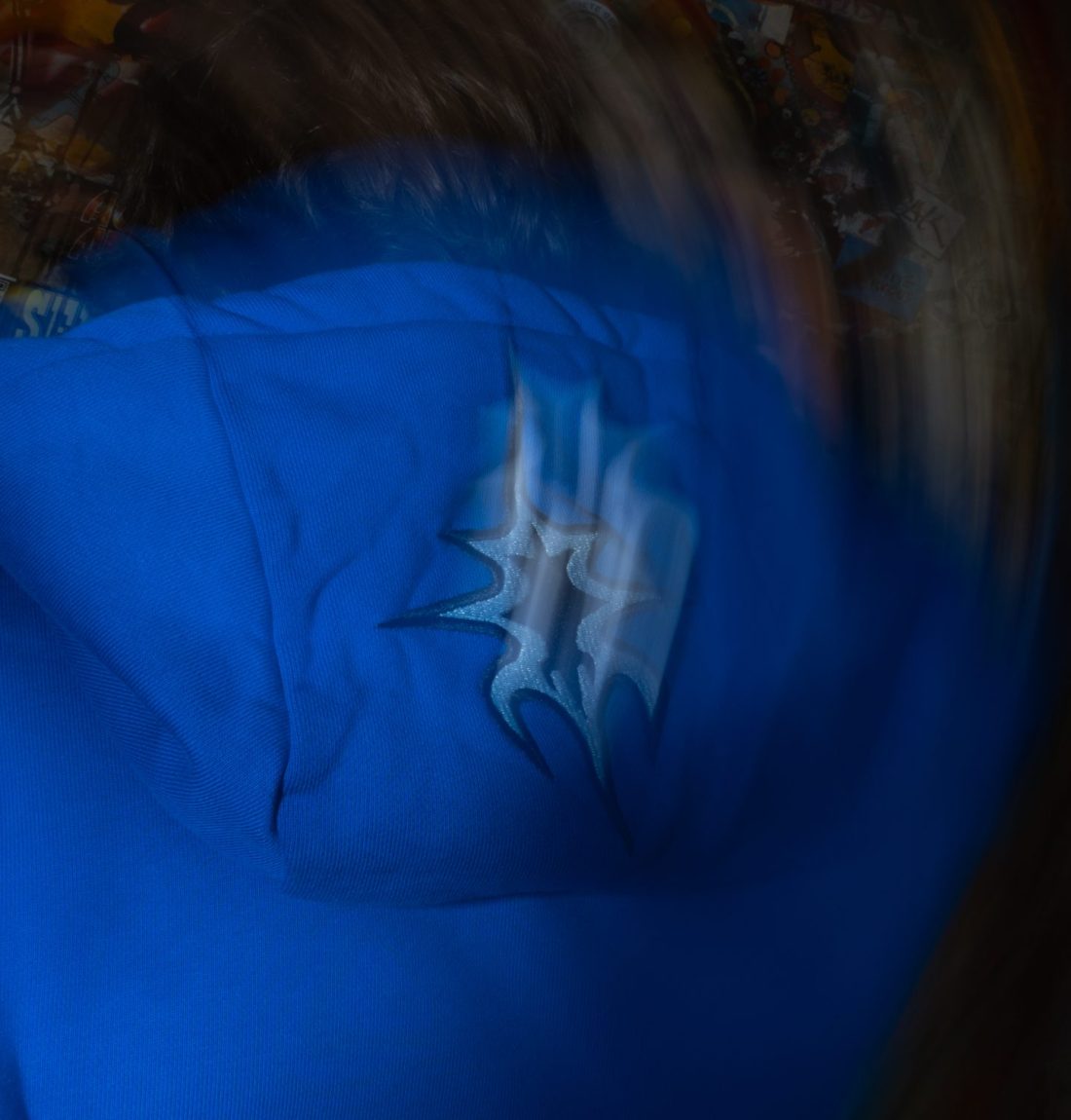 Un très fort flou artistique avec en premier plan le dos d'un homme portant le sweat bleu de la marque citizen. On distingue a peu près le détail de broderie sur la capuche.
