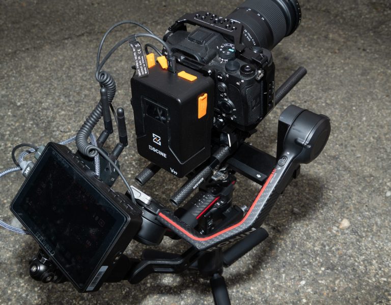 Gros plan sur un stabilisateur DJI Ronin avec caméra Sony, écran externe et câbles; modules et accessoires visibles; sol en béton/granuleux.