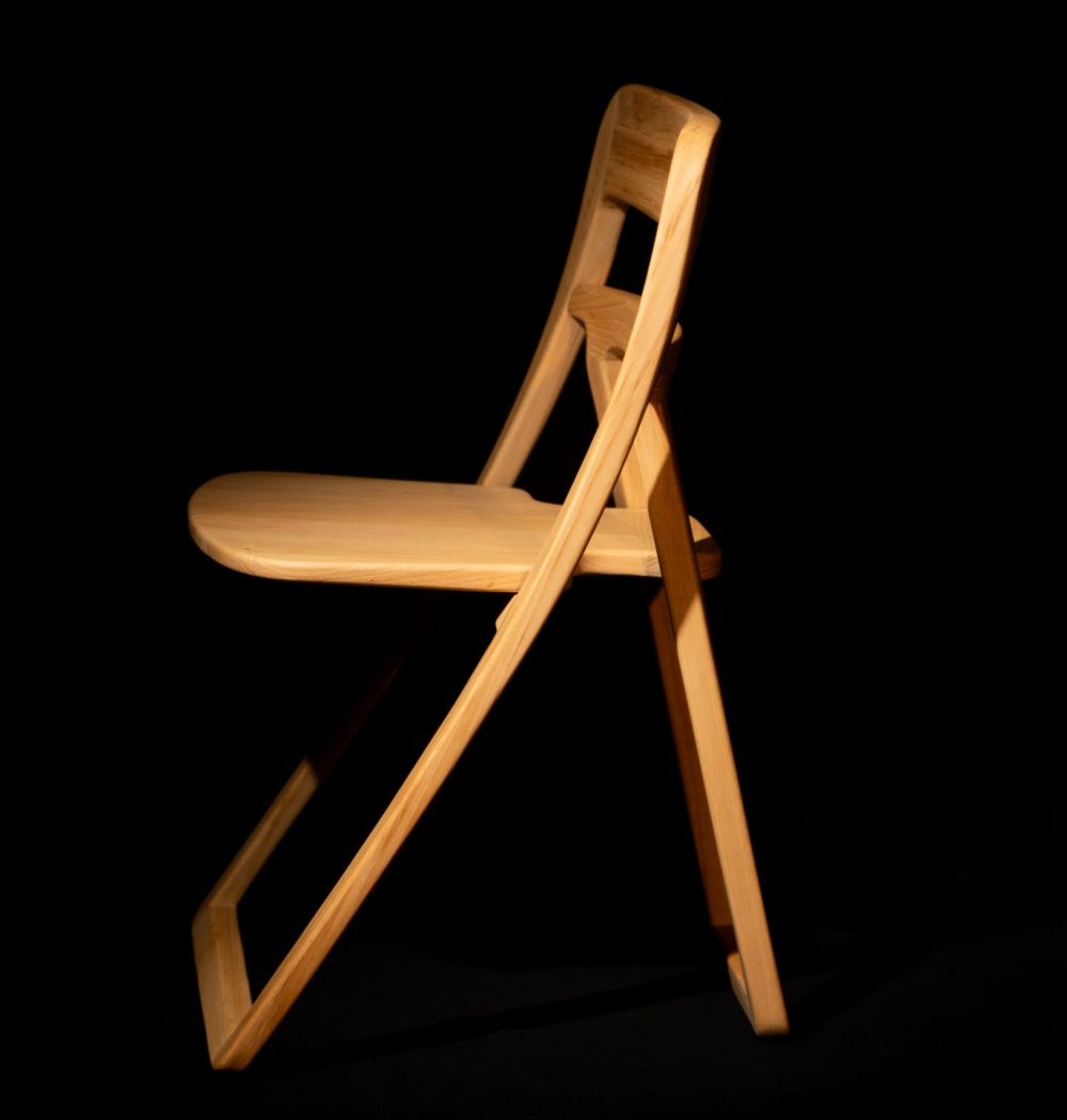 chaise de profil, découpée par la lumière, on voit la finesse du design. la chaise ressort du fond
