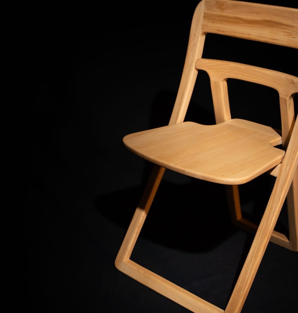 chaise en bois de 3/4 face détachée du fond par le contraste clair et sombre sur fond noir