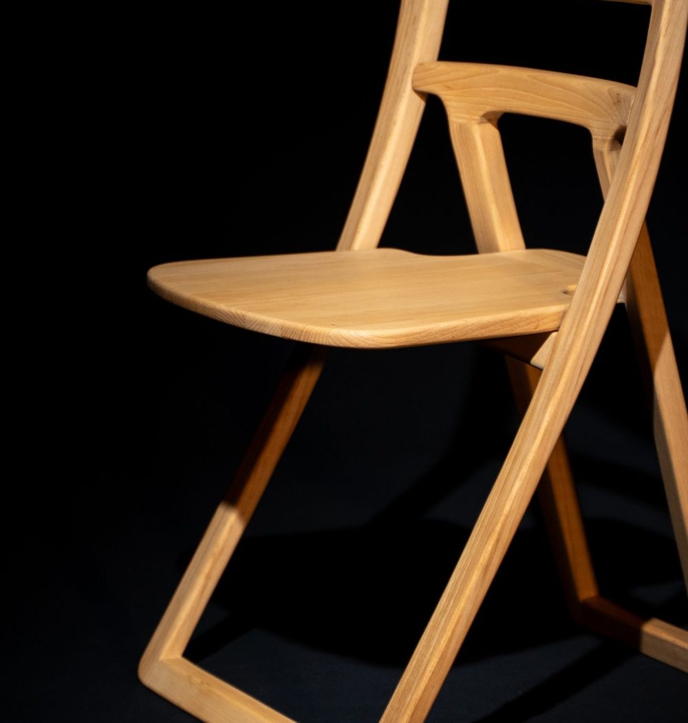 chaise en bois clair pliante, photo au format vertical, qui met en valeur l'architecture de la chaise avec ses longs pieds