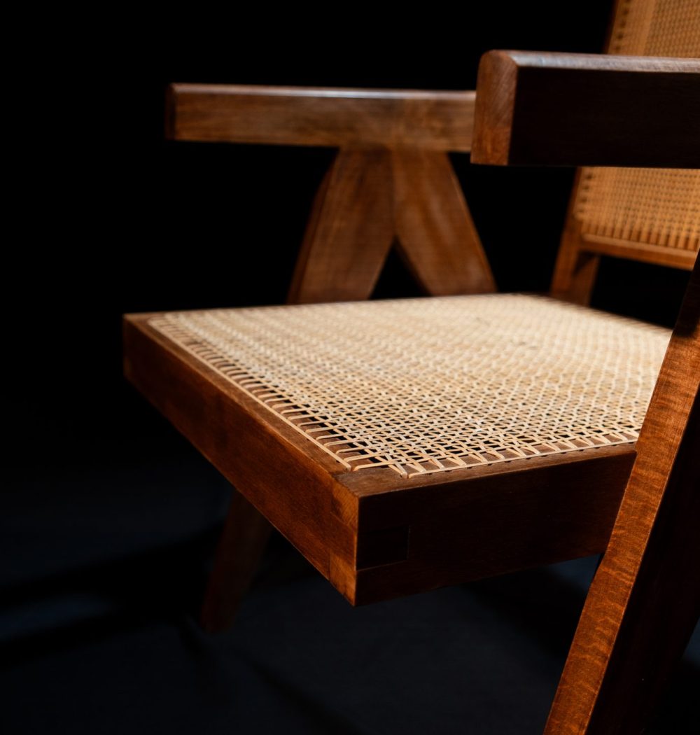 Photo de l'angle de la chaise, châssis en tek un type de bois, on voit le détail du cannage, la chaise est mise en valeur par le fond noir et par la lumière