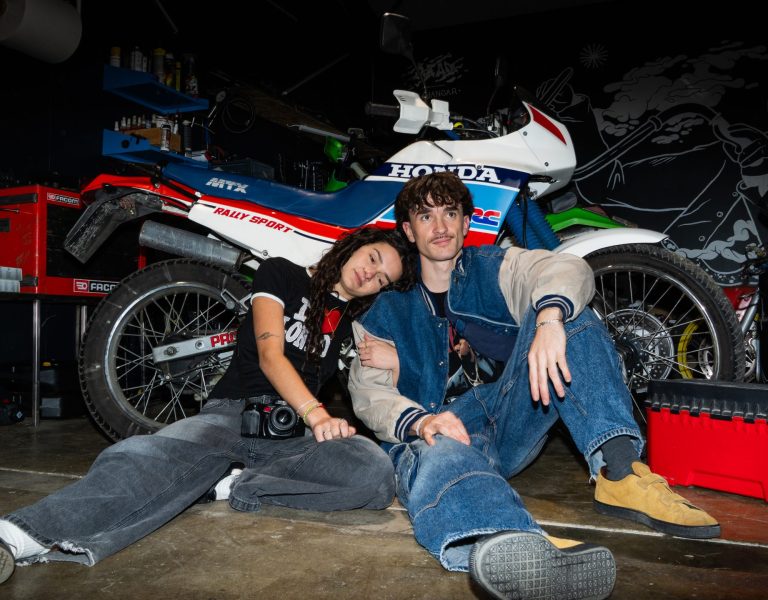 jeune couple habillé de façon vintage, qui pose devant une moto Honda dans un garage sombre